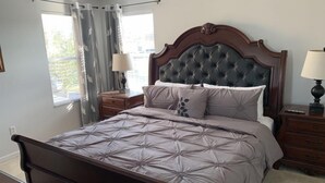 A bedroom with a large bed, two nightstands, a wooden headboard, and a window with curtains. - Terra Verde 693 (Kissimmee)