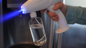 A person holding a spray bottle with a clear liquid, possibly for cleaning or sanitizing, in front of a stainless steel appliance, likely a refrigerator or oven. - Terra Verde 693 (Kissimmee)