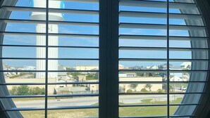 Ventana circular con persianas horizontales, que muestra un edificio alto y zona residencial circundante.