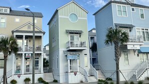 Una hilera de edificios residenciales frente a la playa con balcones, un letrero de alquiler vacacional y una señal de calle que indica el departamento de bomberos.