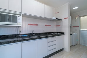 A kitchen with white cabinets, a black countertop, a microwave, and a sink. - Zancanaro 203-Apto 641E (Bombinhas)