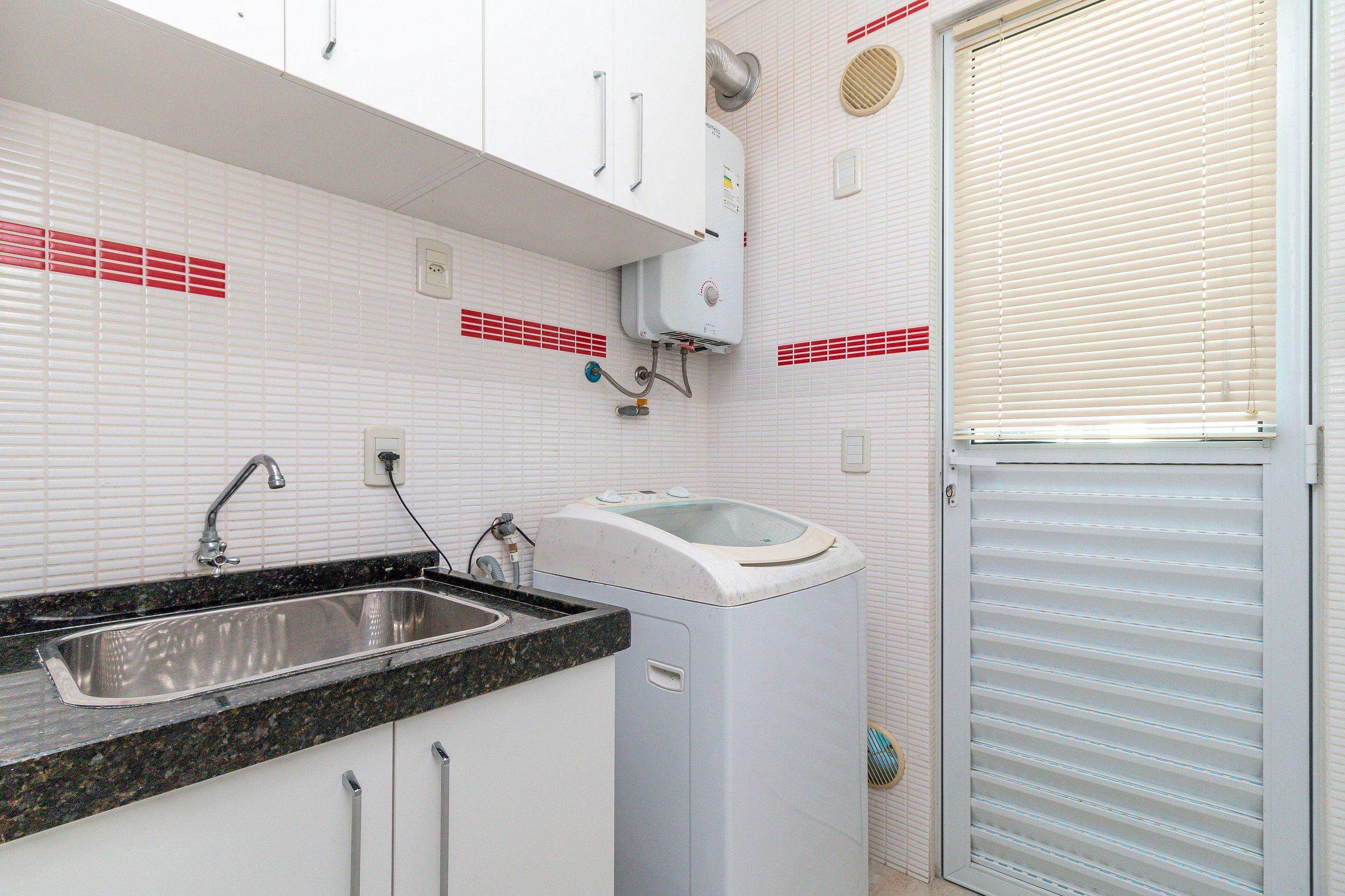 A kitchen with a sink, a washing machine, and a window with blinds.