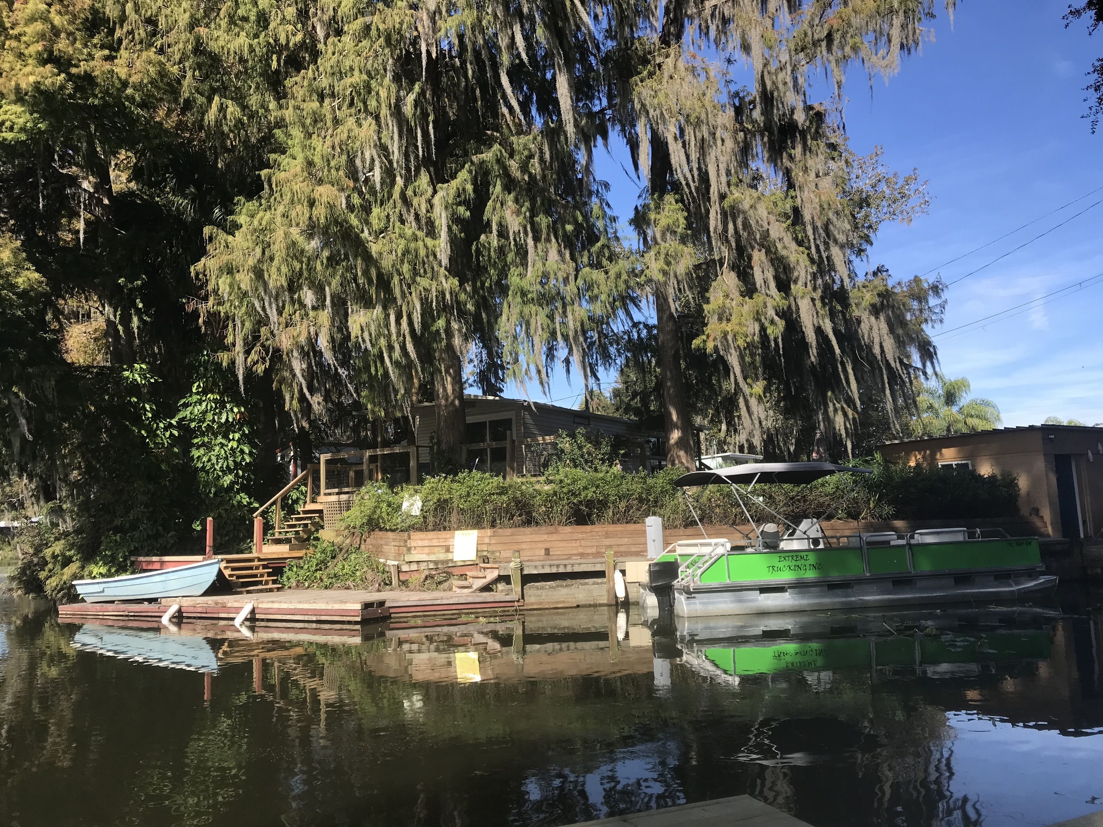 A calm water body with boats docked, surrounded by dense trees and a building with a dock.