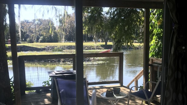 A covered outdoor seating area with a view of a pond and trees. - Waterfront Cottage on the Harris chain in Leesburg  (Leesburg)