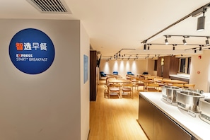 A modern dining area with round tables and chairs, a kitchen counter with stainless steel appliances, and a sign indicating a breakfast service. - Holiday Inn Express Shanghai Baoshan Baoyang by IHG (Shanghai)