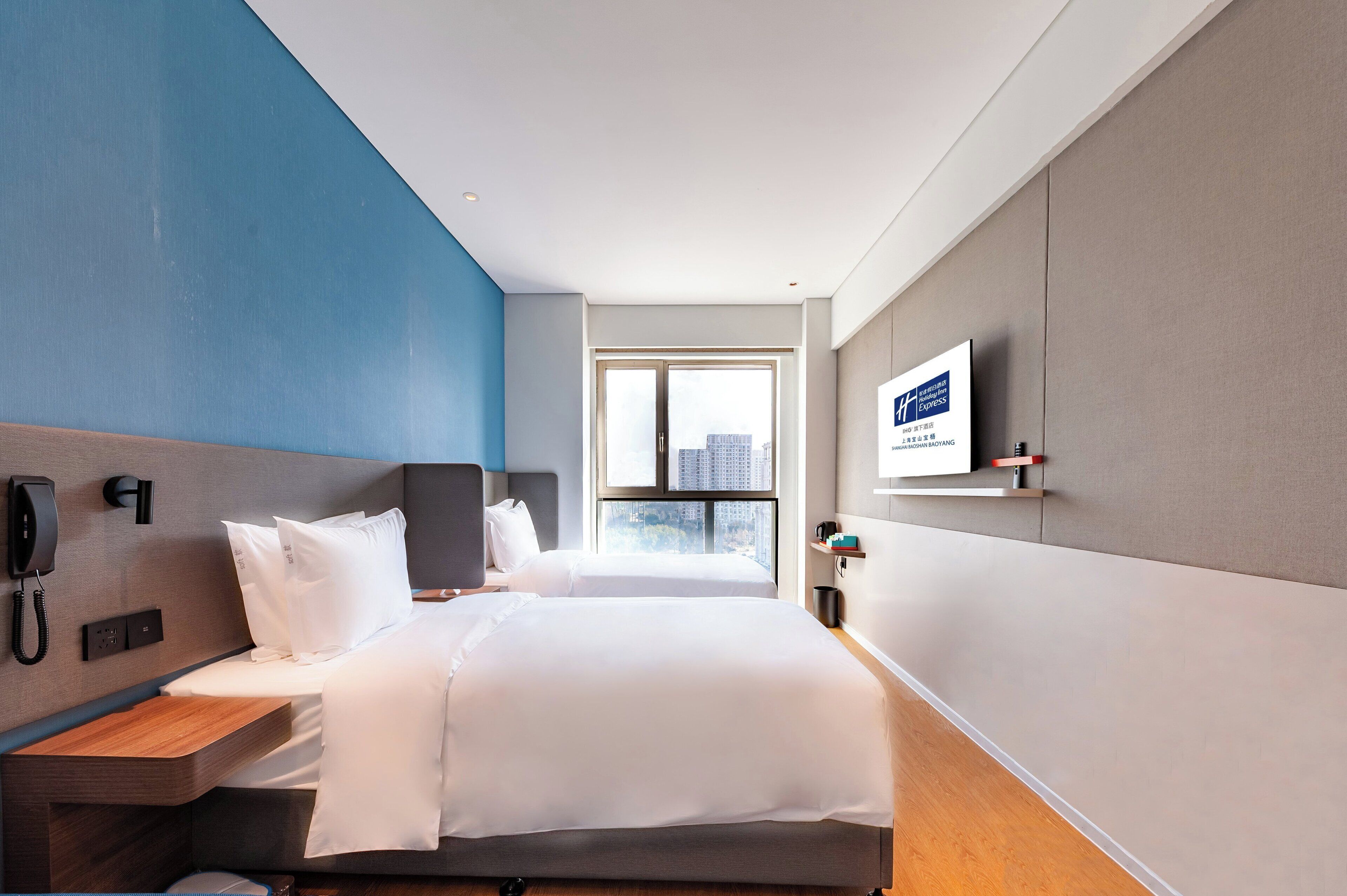 Habitación de hotel con cama, mesita de noche, teléfono y ventana con vista a la ciudad.