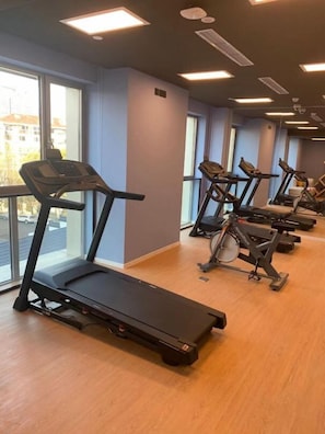 Un gimnasio con cintas de correr y bicicletas estáticas, ventanas amplias y piso de madera.