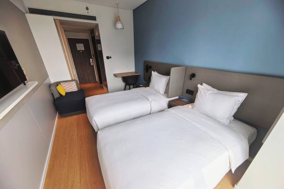 A hotel room with two beds, a desk, a chair, a TV, and a door leading to another room.