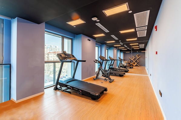 Un gimnasio moderno con cintas de correr, bicicletas estáticas y un espejo grande.