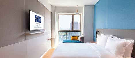 Habitación de hotel con cama, televisor, ventana con vistas a la ciudad y una pared de acento azul.