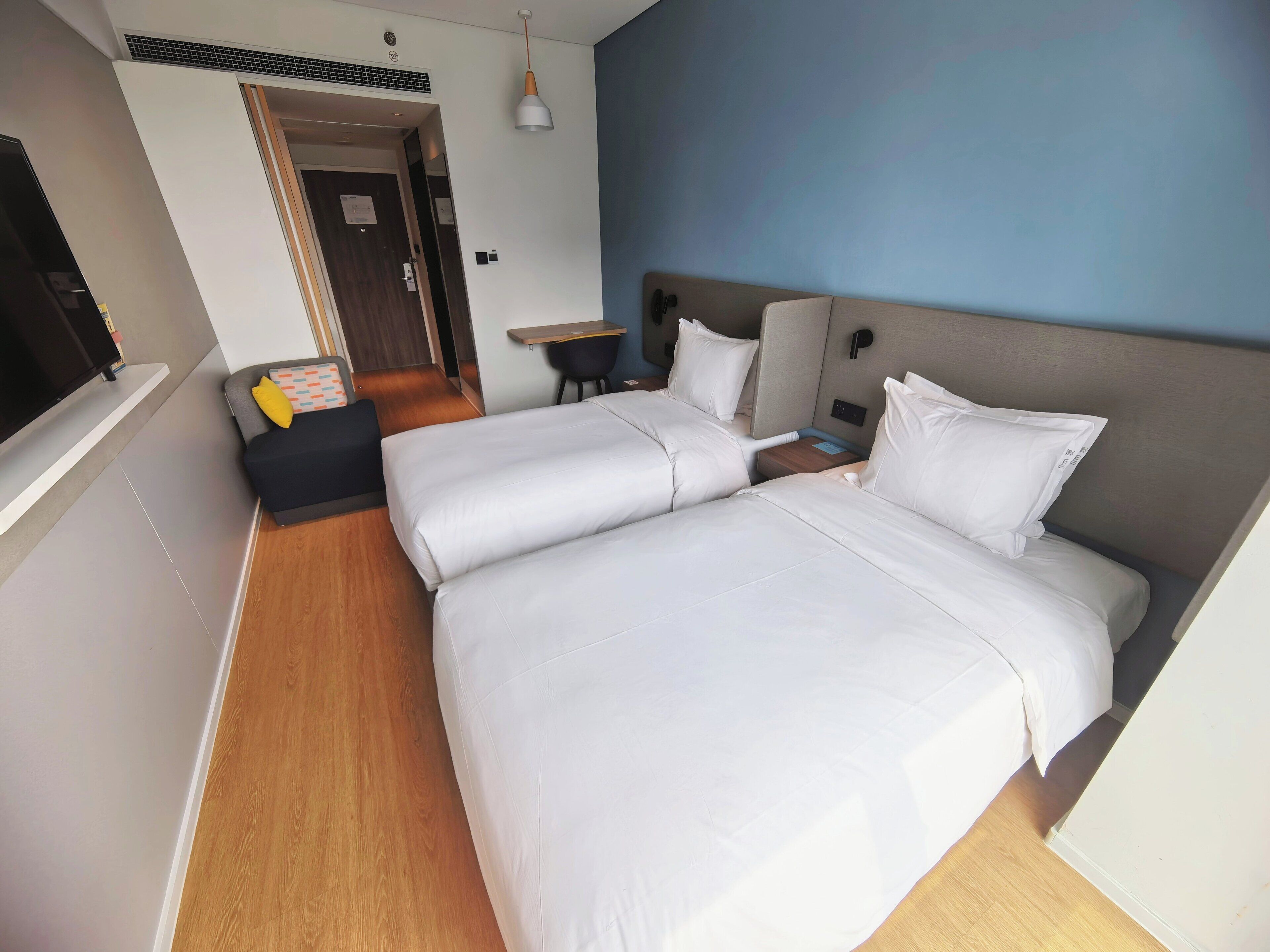 Habitación de hotel con dos camas, un escritorio, una silla, un televisor y una puerta que da a otra habitación.