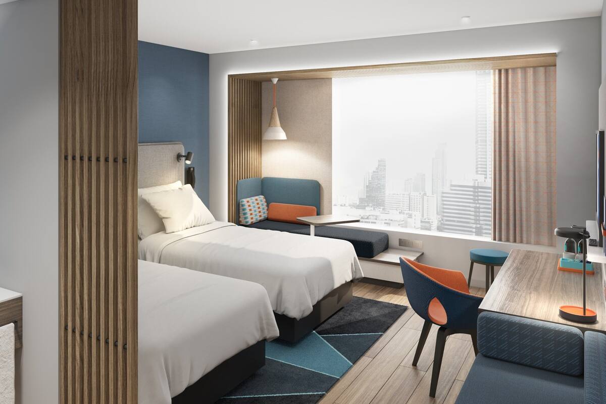 A modern hotel room with two beds, a sitting area, a large window with a city view, a sink, and a mirror.