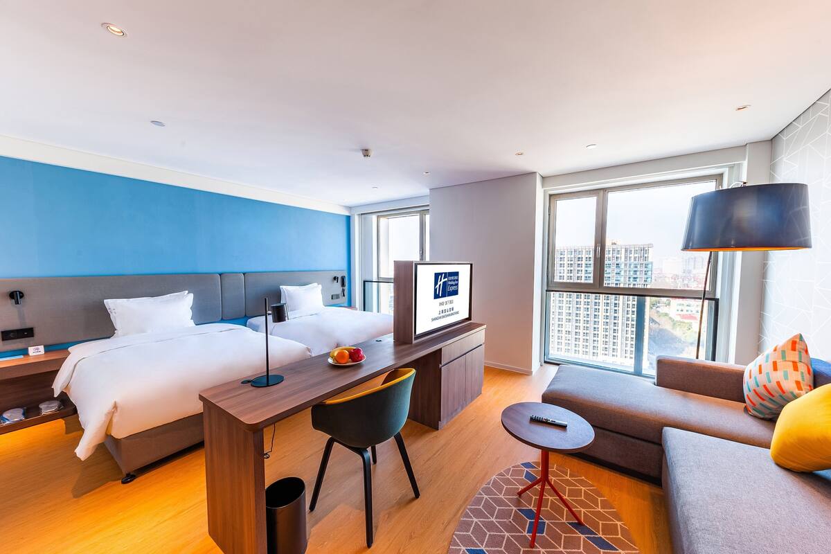 A modern hotel room with a bed, desk, and seating area.
