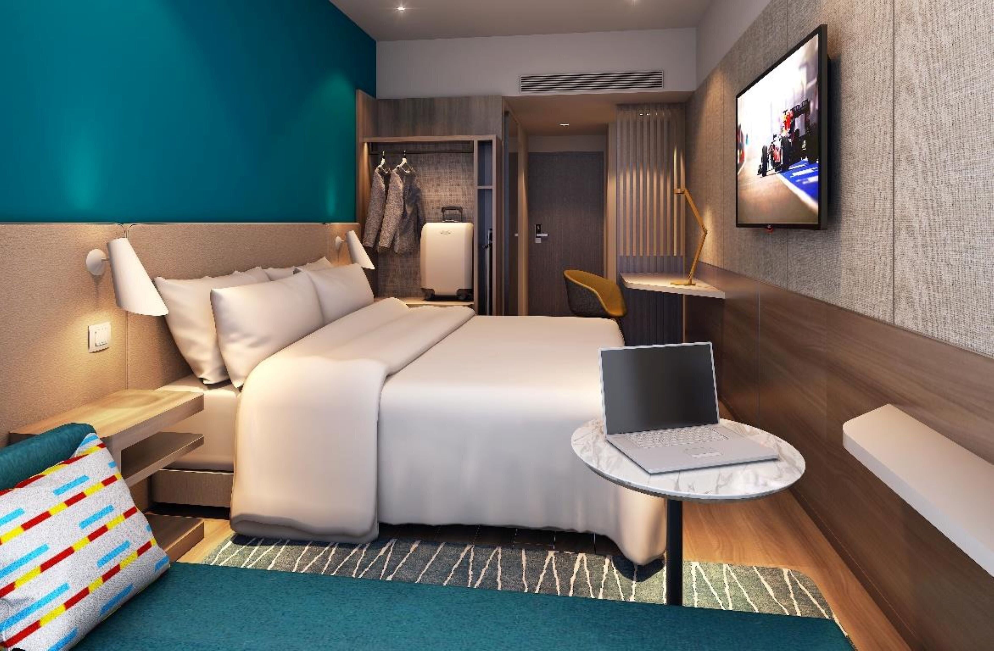 Une chambre d’hôtel moderne équipée d’un lit, d’un bureau avec un ordinateur portable, d’une télévision et d’une armoire.