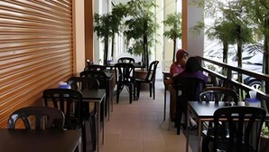 An outdoor cafe with tables and chairs, potted plants, and a covered area with a view of the street. - Hotel Reko Inn (Kajang)
