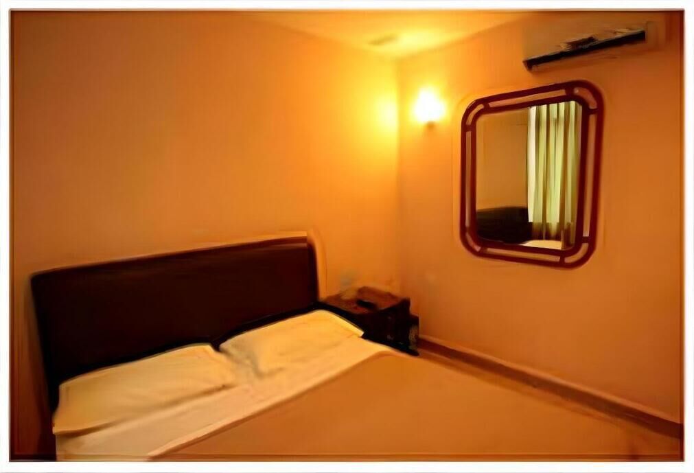 Une chambre d’hôtel avec un lit simple, une table de chevet, un miroir fixé au mur et un luminaire.