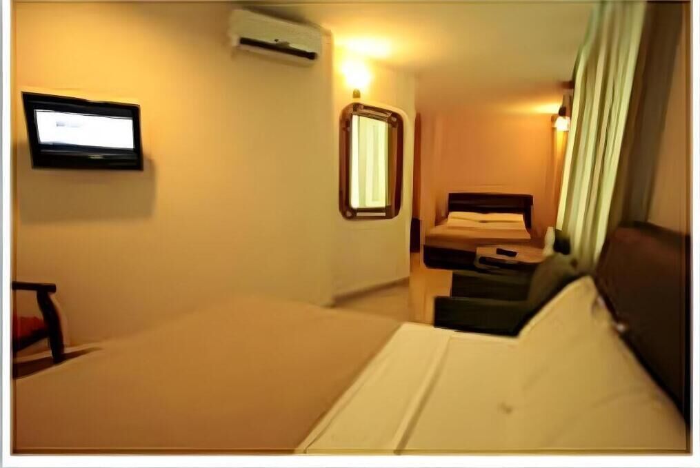 A hotel room with a bed, a desk, a chair, a TV, and an air conditioning unit.