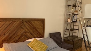 A bedroom with a wooden headboard, a bed with striped bedding, a ladder, and a chair.
