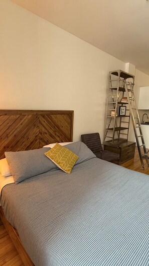 A bedroom with a wooden headboard, a bed with striped bedding, a ladder, and a chair. - Simple and functional loft in the city center (Québec)