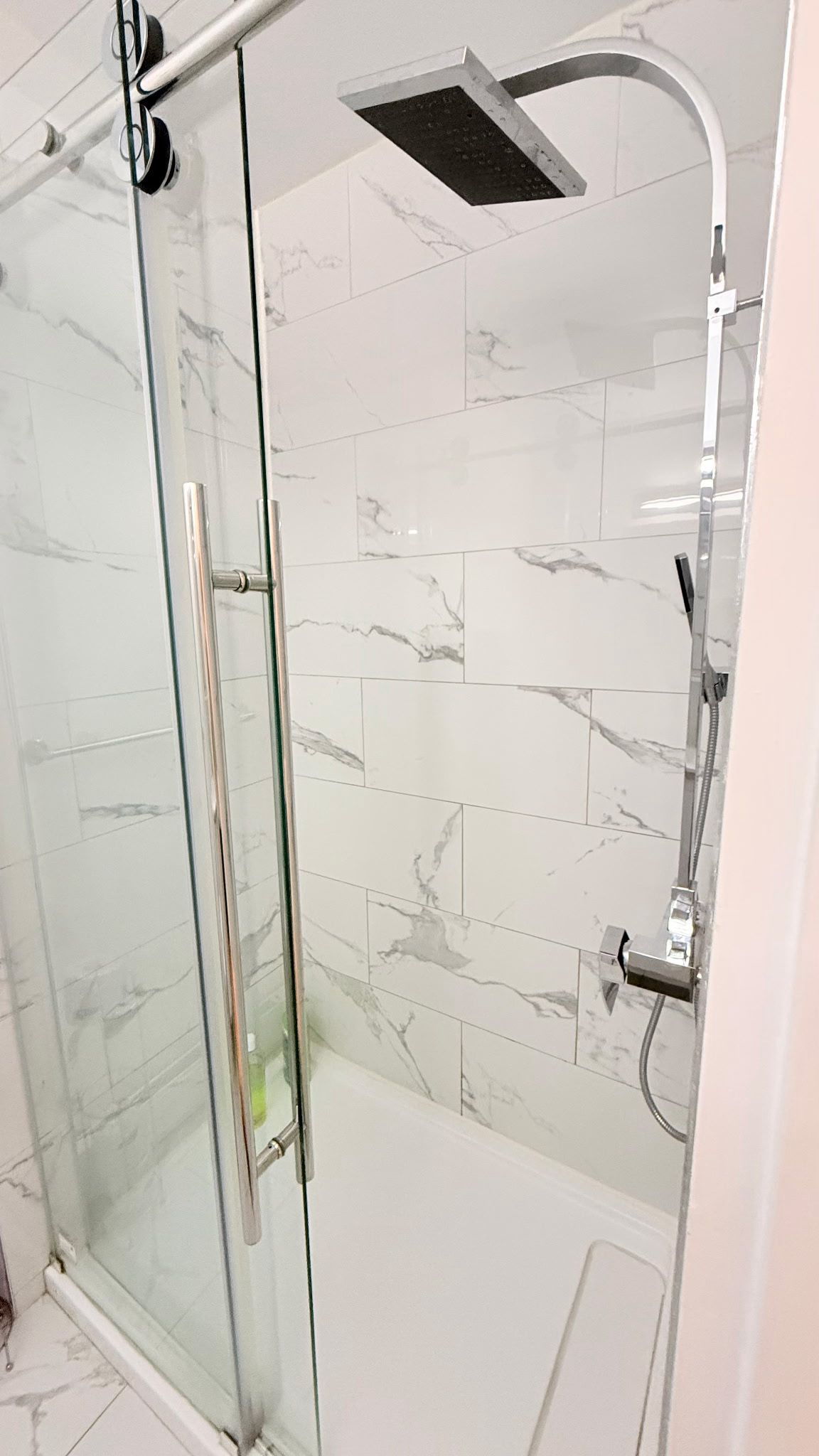 A glass-enclosed shower area with a handheld showerhead and a fixed overhead showerhead.