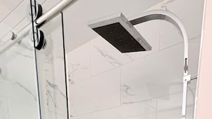 A glass-enclosed shower area with a handheld showerhead and a fixed overhead showerhead.