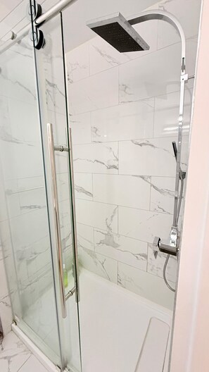A glass-enclosed shower area with a handheld showerhead and a fixed overhead showerhead. - Simple and functional loft in the city center (Québec)