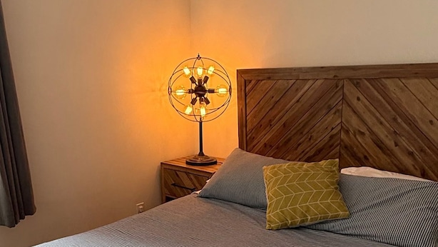 A neatly made bed with a striped bedspread, a wooden headboard, a bedside lamp, and a folded towel on the bed.