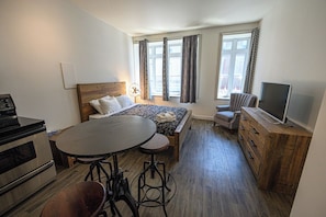 A bedroom with a bed, a TV, a table with stools, a dresser, and a window with curtains.