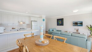 Une cuisine moderne avec des meubles blancs, une cuisinière encastrée et un coin repas comprenant une table et des chaises en bois.