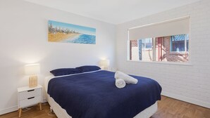 Une chambre à coucher avec un lit, des tables de chevet, une fenêtre donnant sur un beau paysage et un tableau accroché au mur.