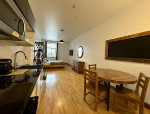 A compact kitchen with a dining area, a bed, and a large window.