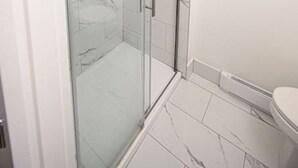 Et moderne badeværelse med brusekabine i glas, hvide marmorfliser og et hvidt toilet.