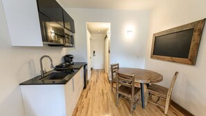 A compact kitchen with a black countertop, wooden flooring, and a dining area with a round table and chairs.