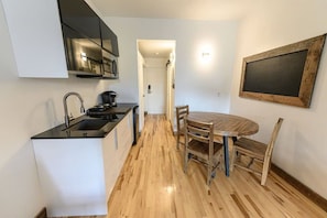 A compact kitchen with a black countertop, wooden flooring, and a dining area with a round table and chairs. - Welcome to Downtown! (Québec)