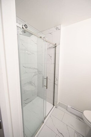 A glass-enclosed shower with a door, a white tiled floor, and a white wall.