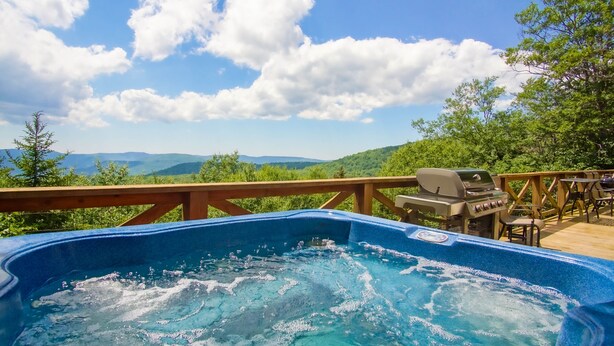 Ein Whirlpool auf einer Holzterrasse mit Blick auf Berge und Bäume.