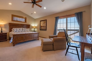 A bedroom with a bed, a chair, a desk, a ceiling fan, and a window with curtains.