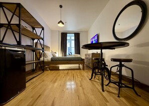 A compact bedroom with a bed, a desk, a chair, a mirror, and a television.