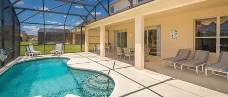 A swimming pool with a glass ceiling, lounge chairs, and a patio area.
