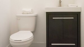 Un bany amb un vàter blanc, un armari fosc i un mirall sobre el lavabo.
