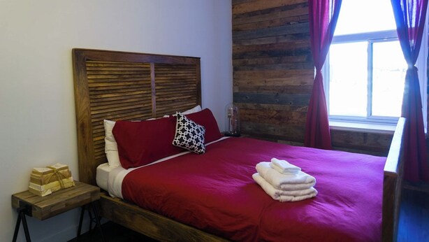 A bed with a wooden headboard, red bedding, and a window with curtains.