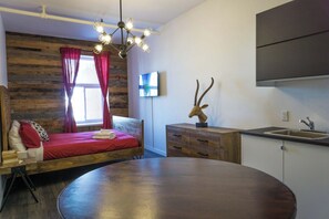 A compact room with a bed, a dining table, a wooden cabinet, a sink, and a mounted television. - Loft douillet au centre-ville ! (Québec)