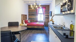 A compact room with a bed, a dining table, a kitchen area, and a window with curtains.