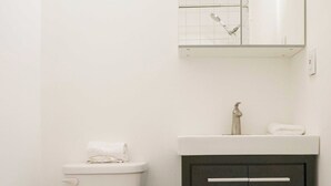 A bathroom with a toilet, a dark cabinet with a mirror, and a white sink.