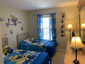Une chambre avec deux lits, des rideaux bleus et une décoration sur le thème des personnages de « Moi, moche et méchant ».