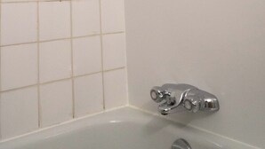 Une salle de bain avec une baignoire, une douche et des murs recouverts de carreaux blancs.