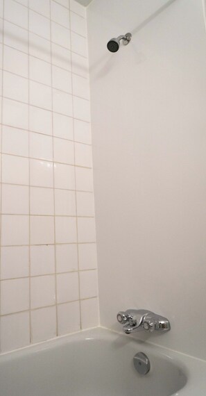 Une salle de bain avec une baignoire, une douche et des murs recouverts de carreaux blancs.