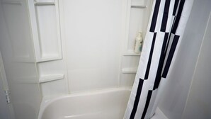A bathroom with a white bathtub, a black and white striped shower curtain, and a white bottle on a shelf.