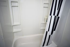 A bathroom with a white bathtub, a black and white striped shower curtain, and a white bottle on a shelf.