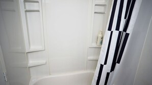A bathroom with a white bathtub, a black and white striped shower curtain, and a shelf with toiletries. - Intimate loft in the heart of the city (Québec)